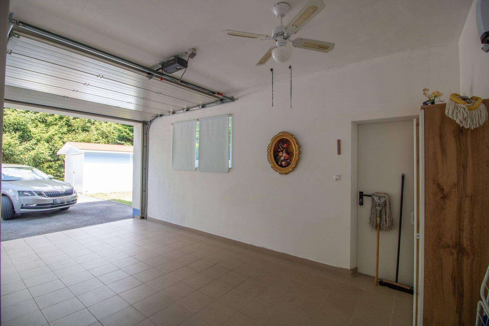 Geräumige Garage mit Fliesenboden, Deckenventilator und direktem Zugang zum Außenbereich.