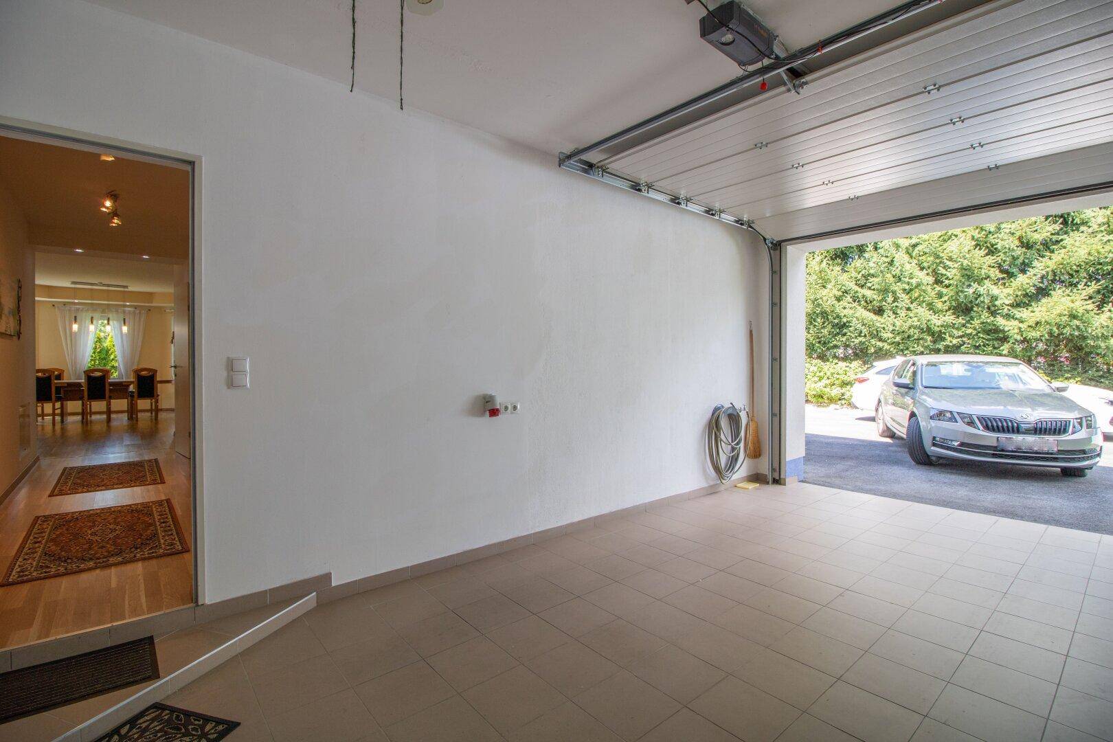 Helle Garage mit Fliesenboden und offenem Tor, das den Blick auf die Einfahrt freigibt.