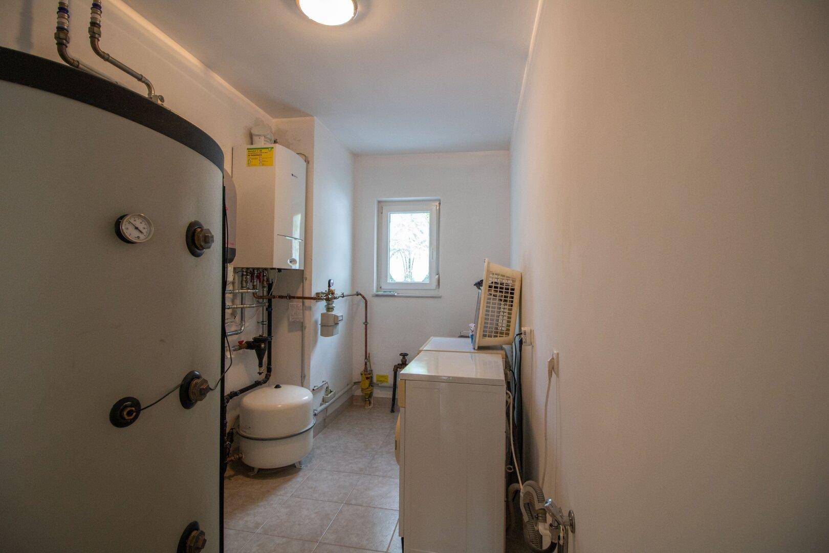 Heller Hauswirtschaftsraum mit Heizungsanlage, Waschmaschine und Fenster.
