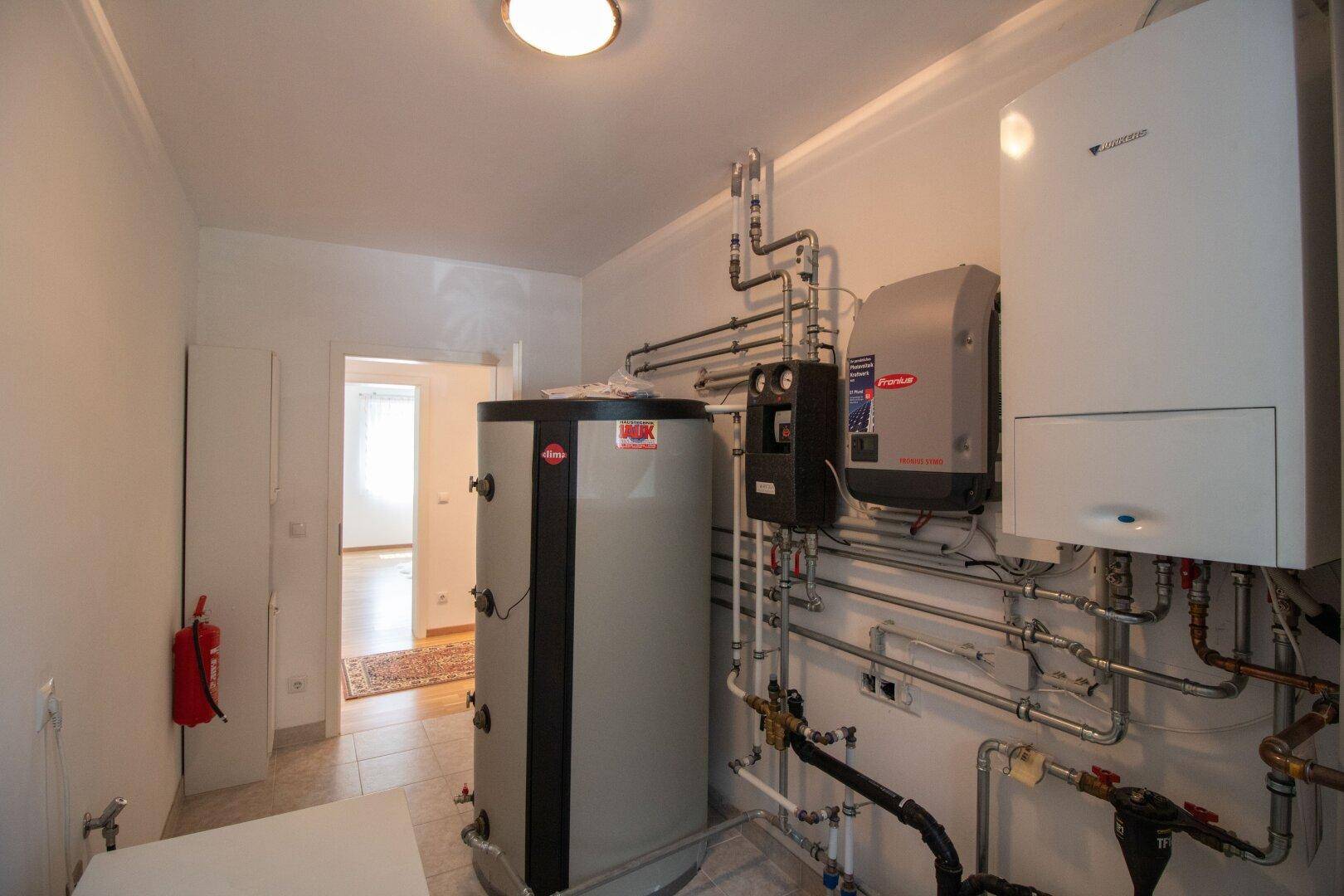 Technikraum mit Heizungsanlage, Warmwasserspeicher und komplexen Rohrsystemen.