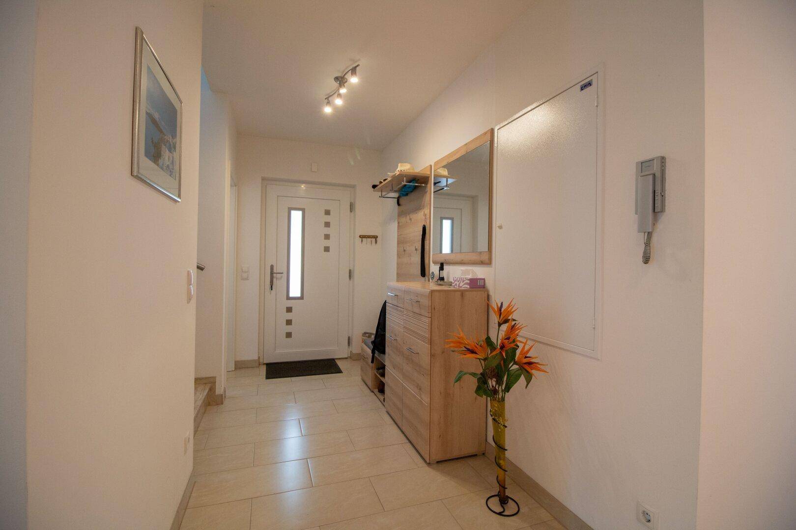 Freundlicher Eingangsbereich mit heller Fliese, Garderobe und Spiegel, einladend gestaltet.