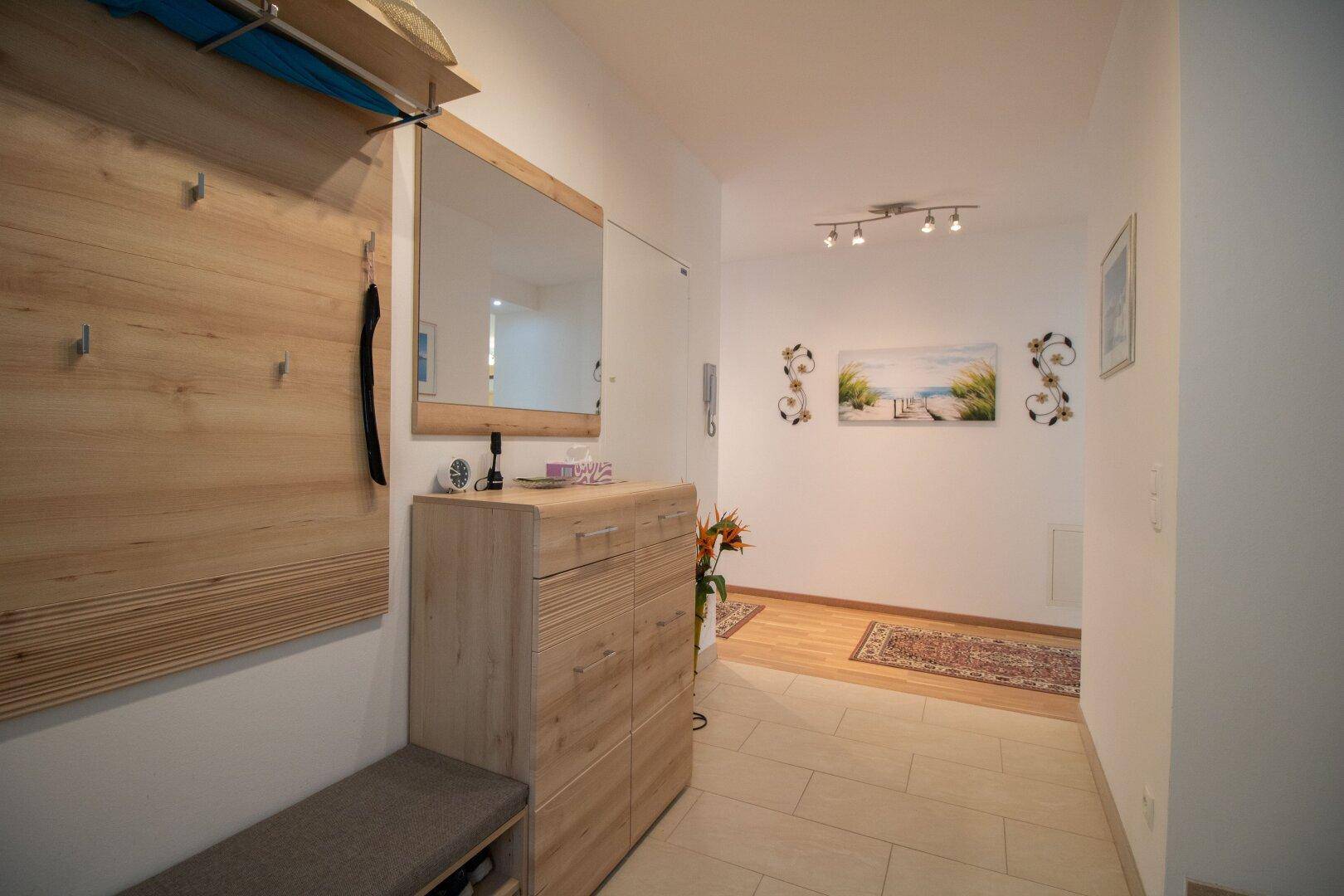 Heller Flur mit Garderobe, Spiegel und dekorativen Elementen, der zu den Wohnbereichen führt.
