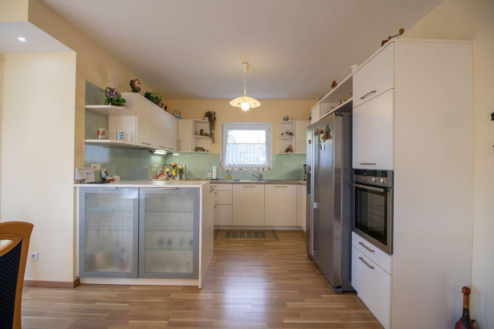 Moderne Einbauküche mit weißen Schränken, integrierten Geräten und Parkettboden.