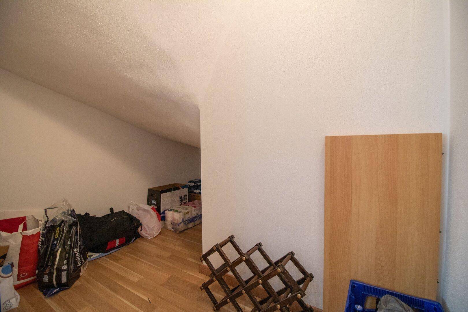 Abstellraum im Dachgeschoss mit schrägen Wänden und Holzregal für zusätzlichen Stauraum.