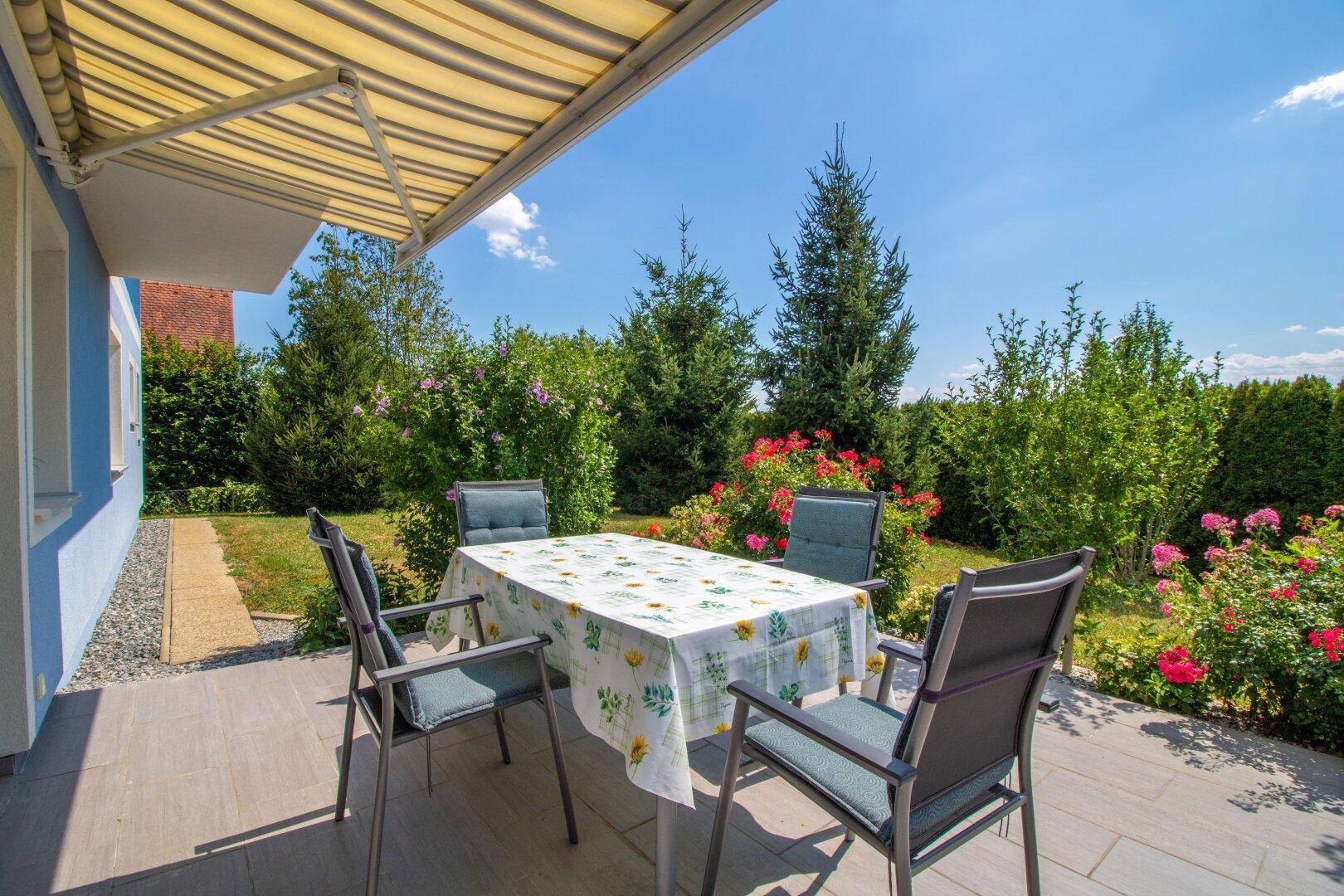 Sonnige Terrasse mit Markise, Gartenmöbeln und Blick ins Grüne.