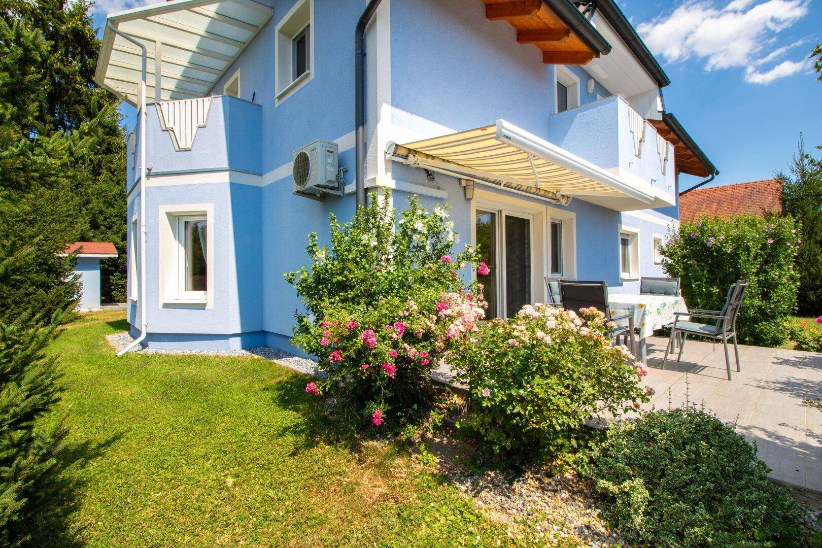 Sonniger Terrassenbereich mit Markise, Gartenmöbeln und blühenden Pflanzen.