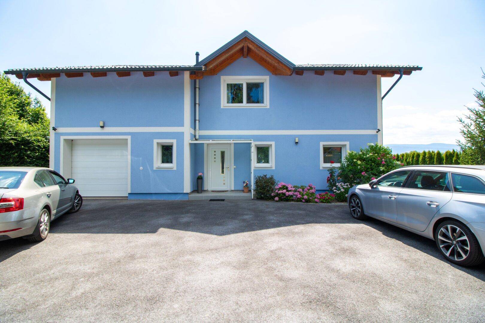 Vorderansicht des blauen Hauses mit Garage und Stellplätzen.