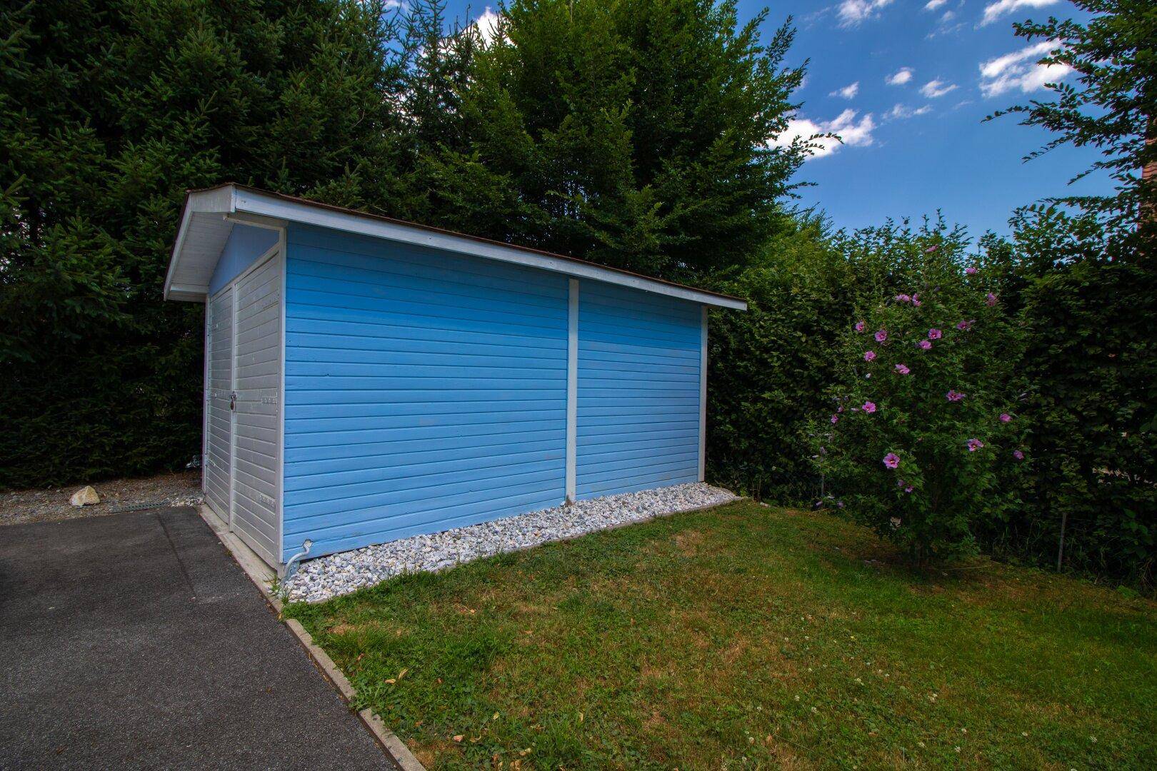 Seitenansicht des blauen Gartenhauses umgeben von Grünflächen.