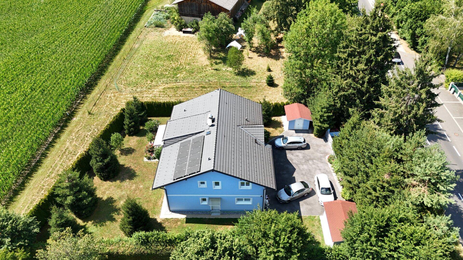 Draufsicht des Hauses mit Photovoltaikanlage, Parkplätzen und angrenzendem Feld.