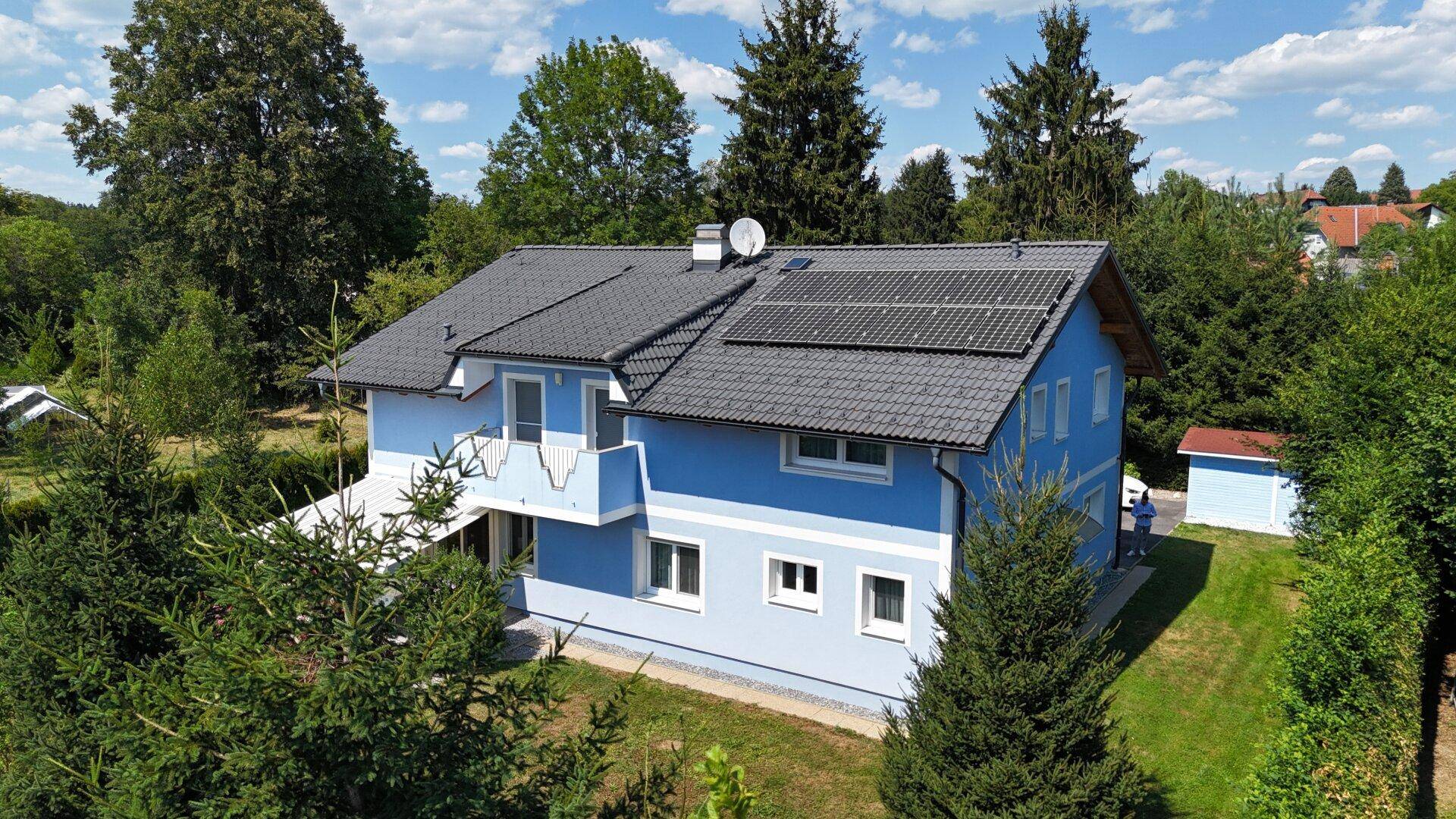 Haus mit Photovoltaikanlage auf dem Dach, umgeben von Bäumen und Grünflächen.