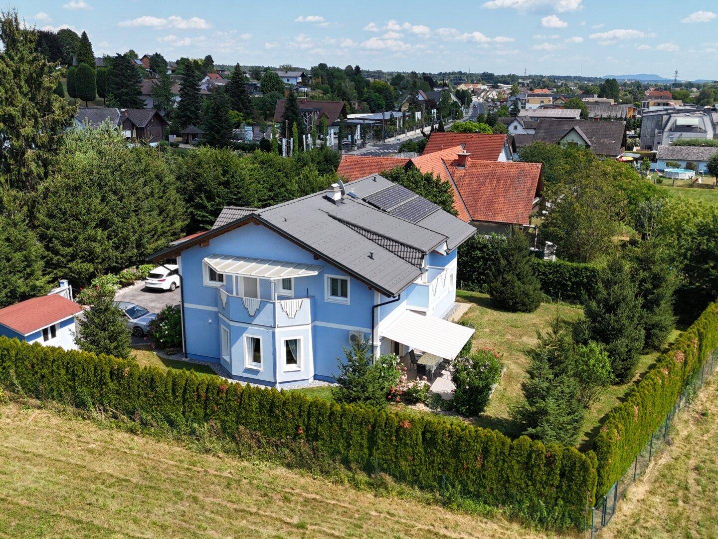 Luftaufnahme des blauen Hauses mit Photovoltaik und gepflegtem Gartenbereich.