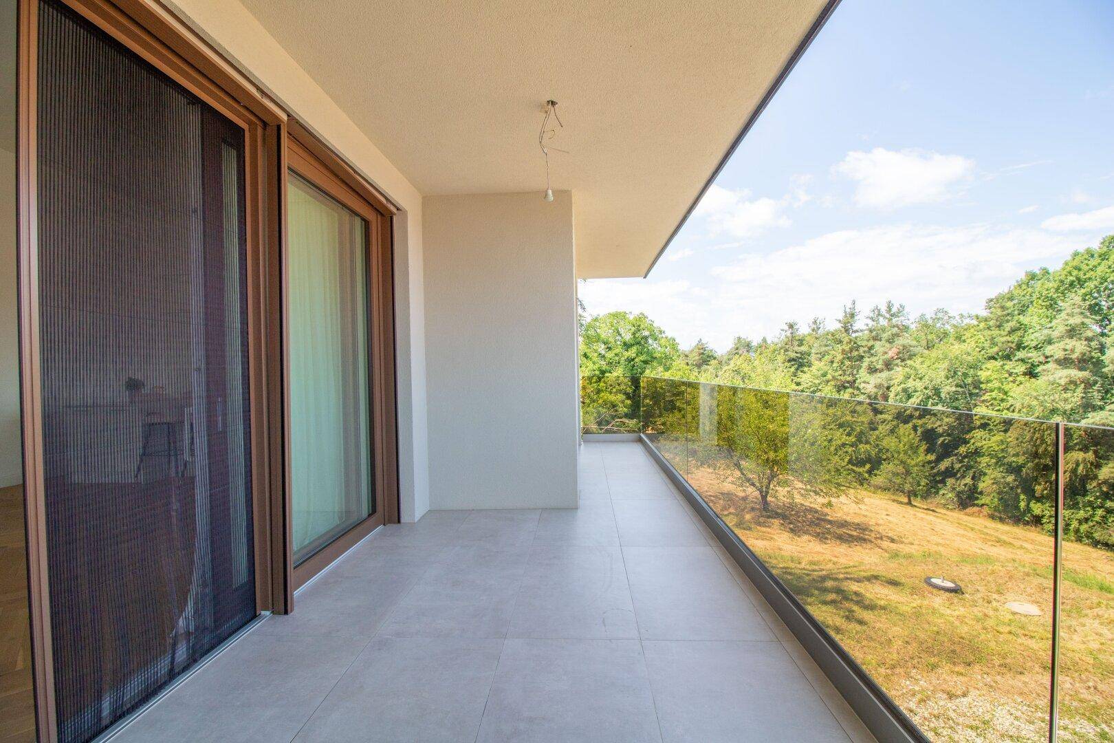 Geräumiger Balkon mit Glasgeländer und weitem Blick über die grüne Landschaft.