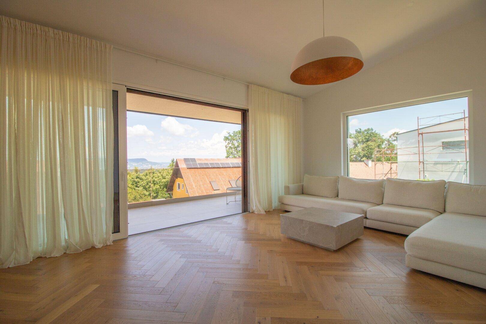 Lichtdurchflutetes Wohnzimmer mit Parkettboden, moderner Einrichtung und Zugang zur Terrasse.
