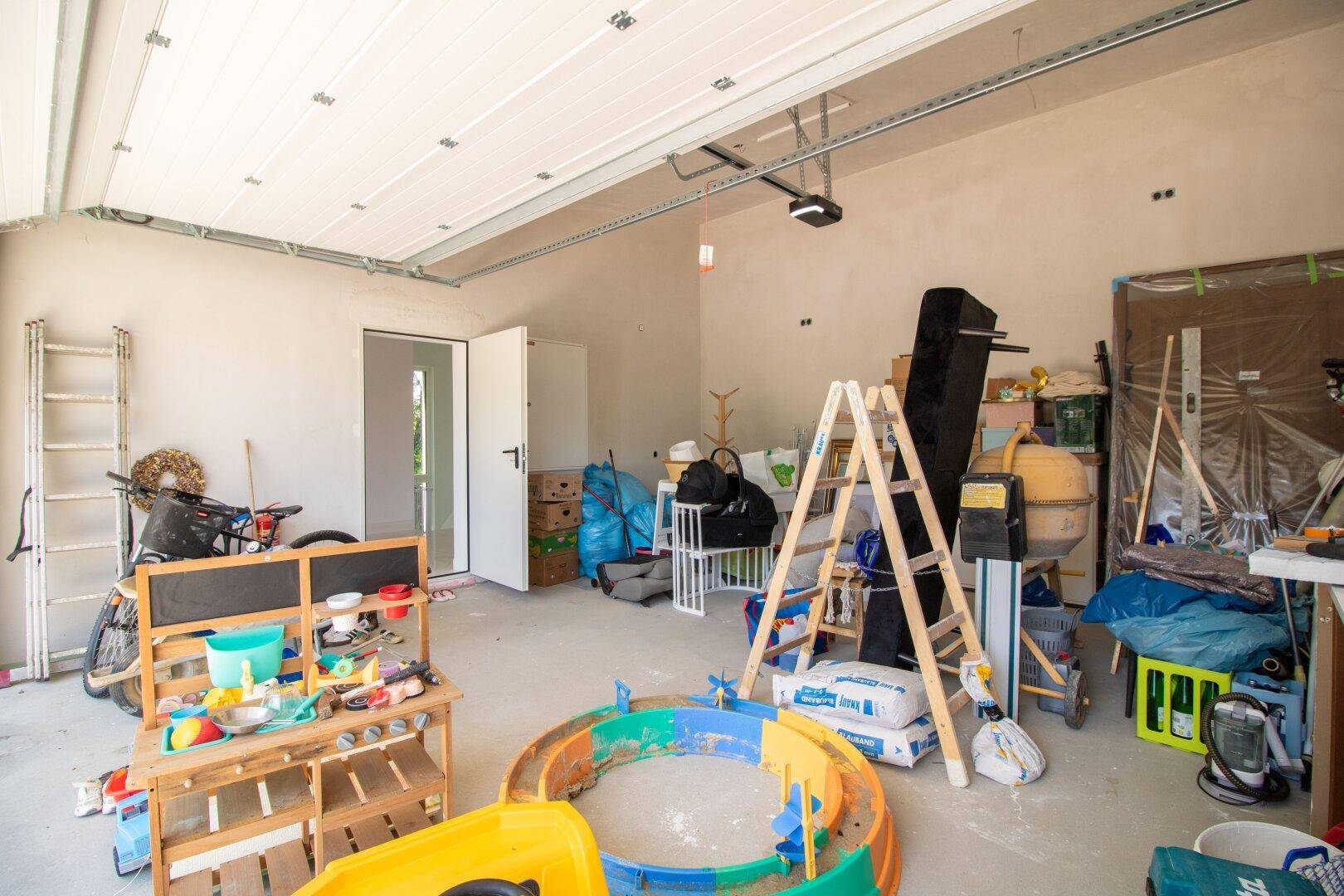 Geräumige Garage mit vielen Gegenständen, darunter Spielzeug, Leitern und Baumaterialien.