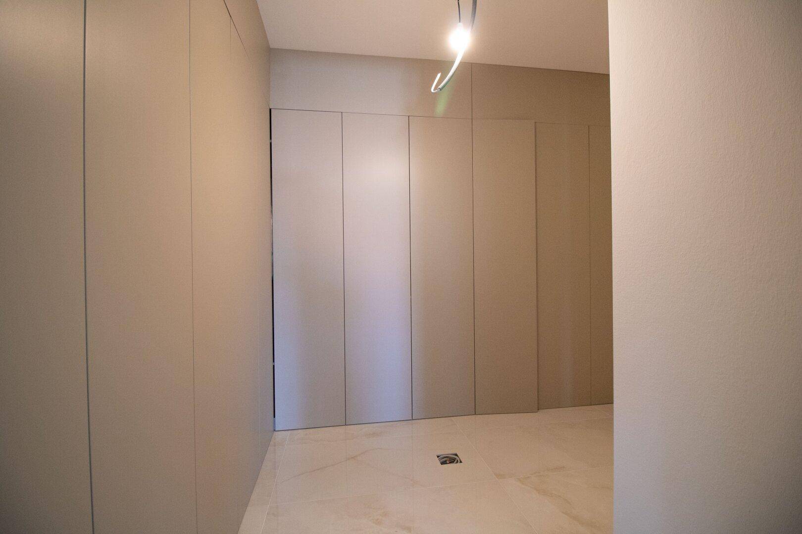 Flur oder Ankleidebereich mit integrierten, schlichten Einbauschränken und Fliesenboden.