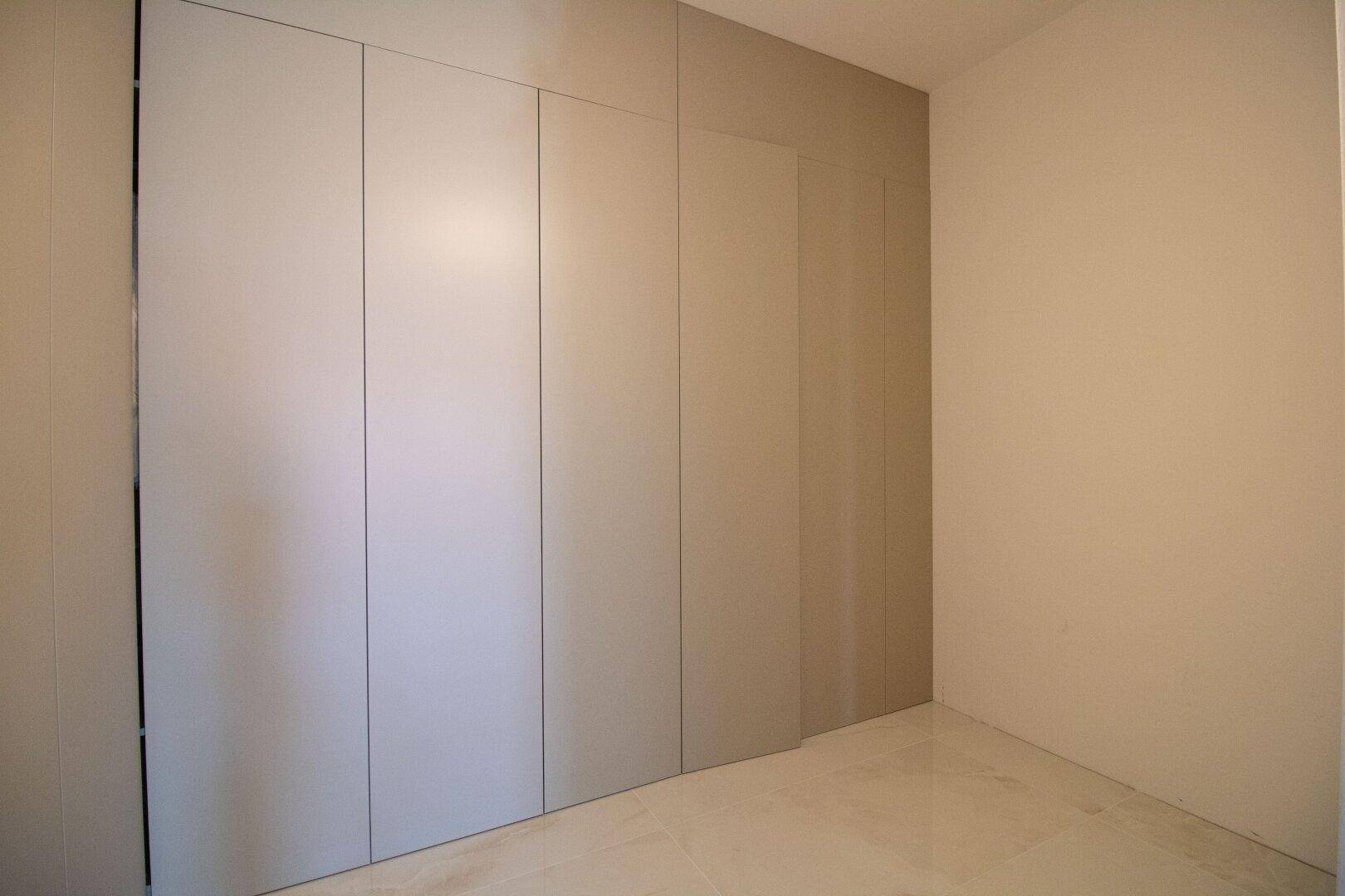 Moderner Flur mit raumhohen Einbauschränken in neutralem Farbton und Fliesenboden.