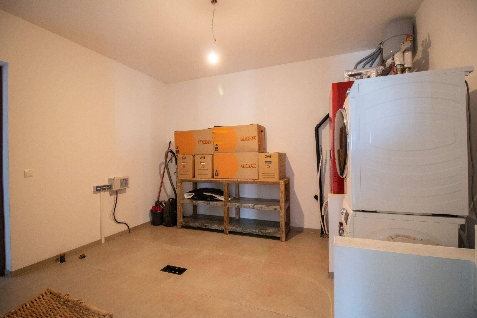 Hauswirtschaftsraum mit Waschmaschine, Trockner und Regalen für Lagerung.