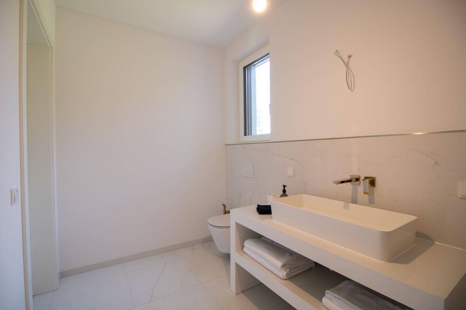 Helles Badezimmer mit modernem Waschtisch, wandhängendem WC und Fenster für Tageslicht.