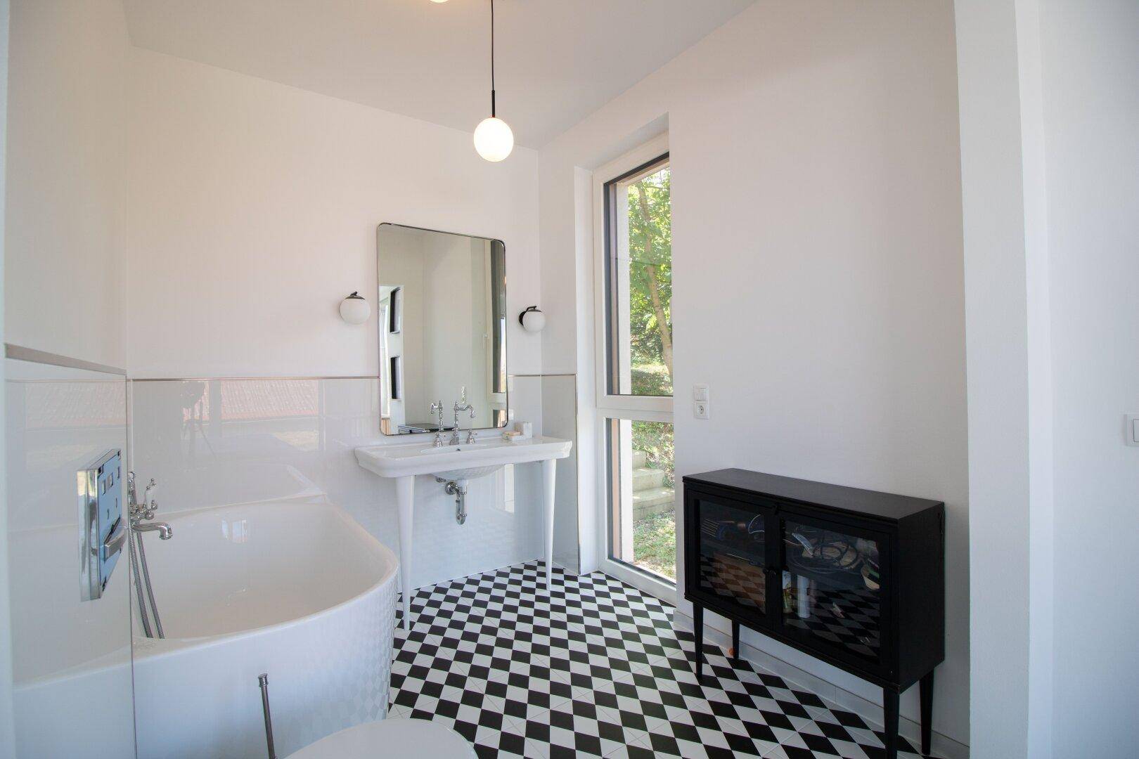Badezimmer mit markantem Schachbrettmuster-Fliesenboden, Badewanne und Fenster.