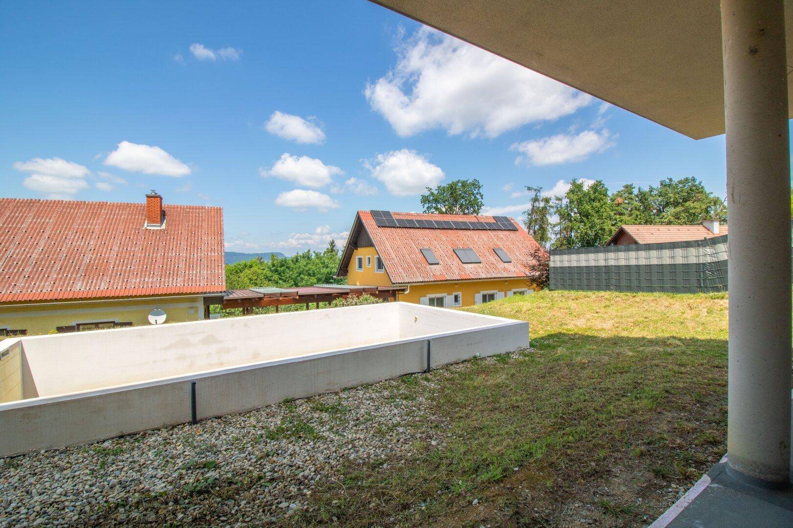 Gartenbereich mit vorbereitetem Poolbecken und Blick auf umliegende Häuser und Natur.