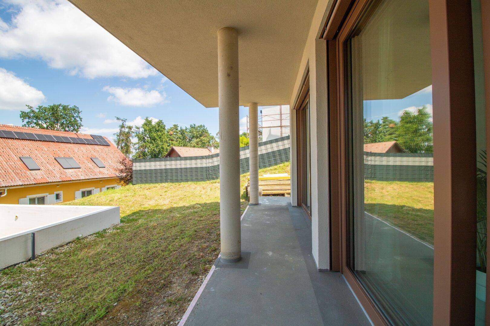Überdachte Terrasse mit Säulen und Blick auf den Garten und die umliegende Landschaft.