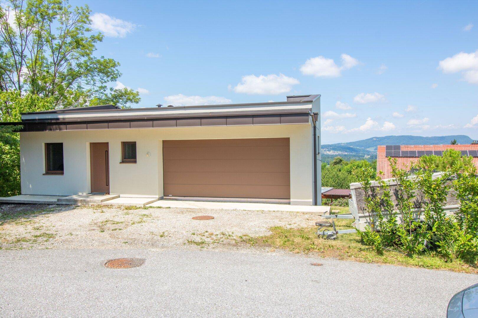Neubau mit Garage und moderner Architektur, eingebettet in eine grüne Hügellandschaft.