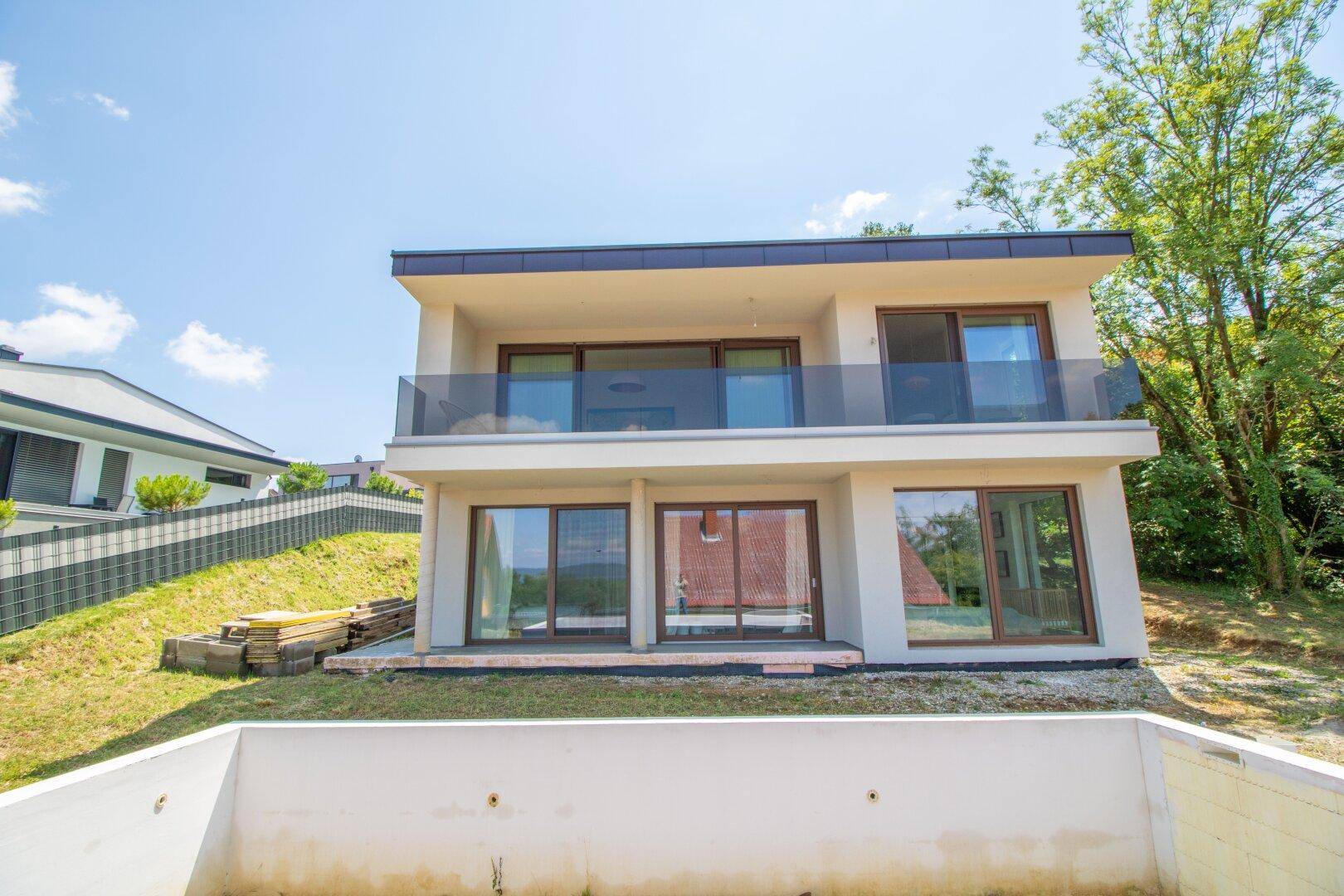 Rückansicht eines modernen Hauses mit Balkonen, großen Fenstern und Poolvorbereitung.
