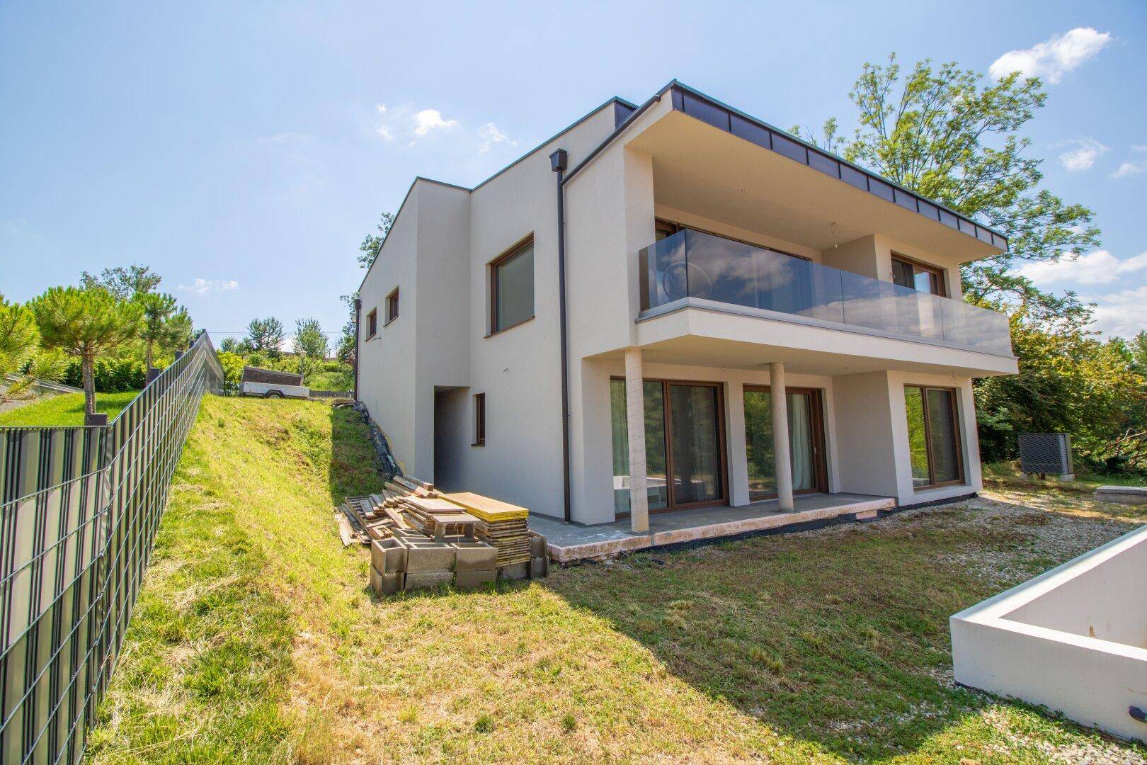 Seitliche Ansicht des modernen Neubaus mit Balkon, großen Fenstern und Gartenbereich.