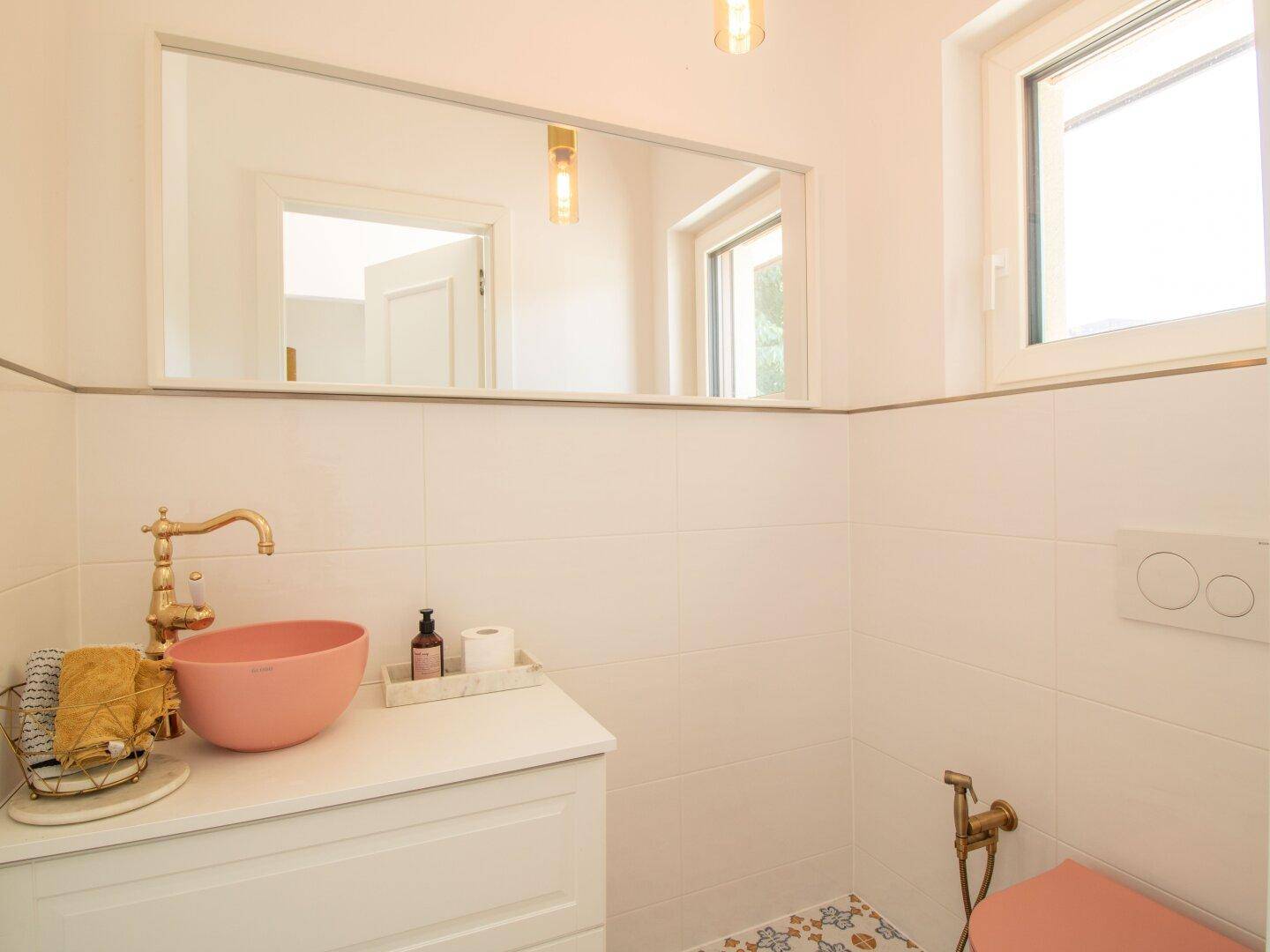 Modernes Gäste-WC mit rosa Waschbecken, Wand-WC und Fenster für Tageslicht.