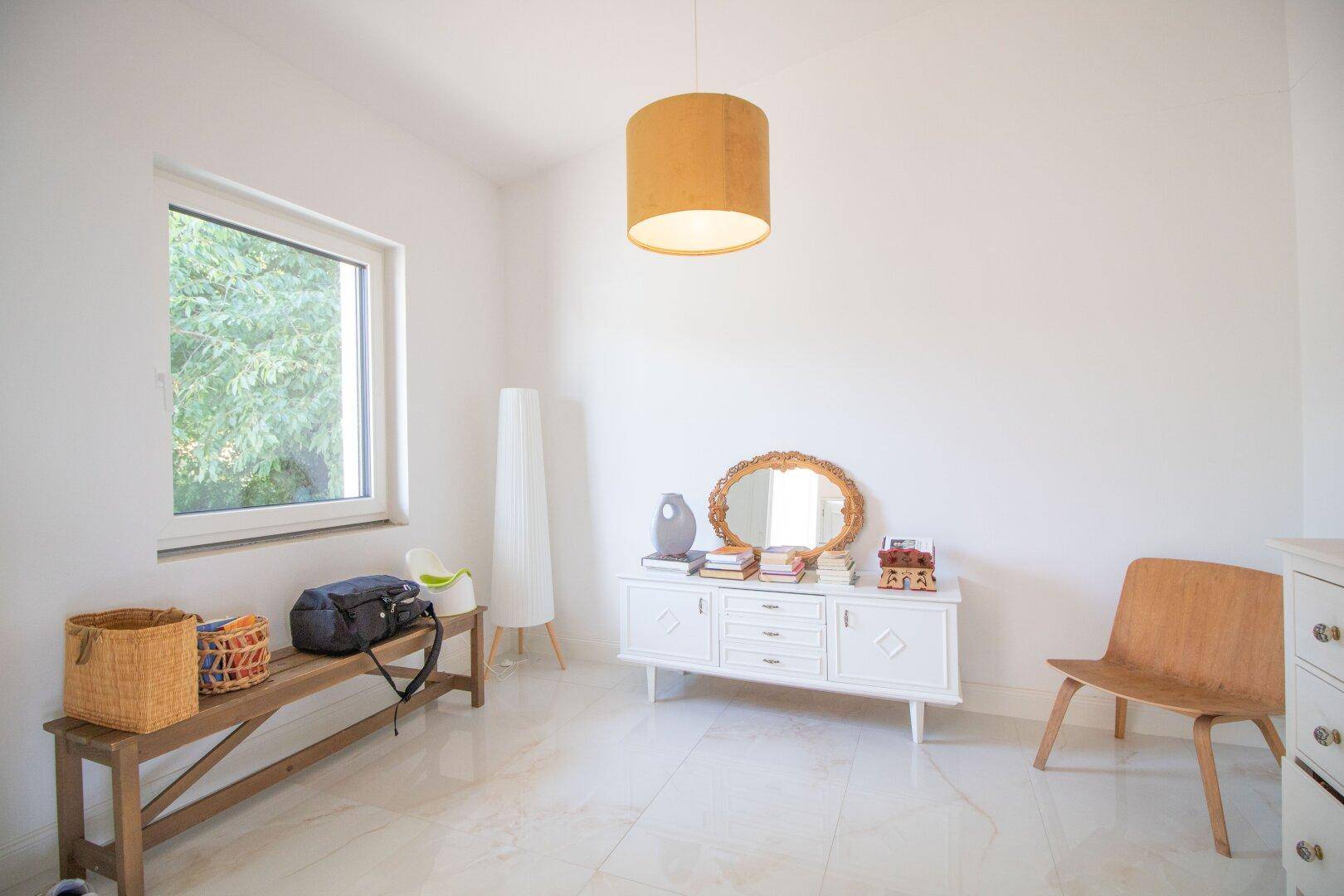 Heller Raum mit Fenster, Fliesenboden und stilvollen Möbeln, ideal als Gästezimmer.