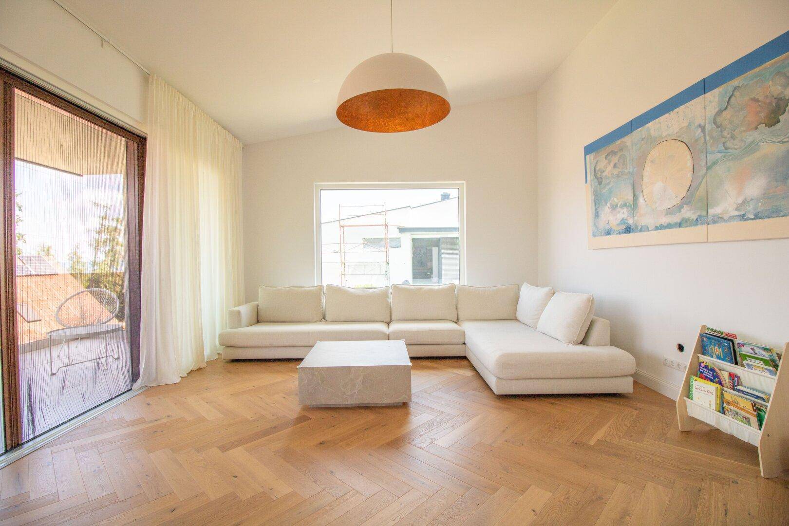 Modernes Wohnzimmer mit Fischgrätparkett, großem Sofa und Zugang zum Außenbereich.