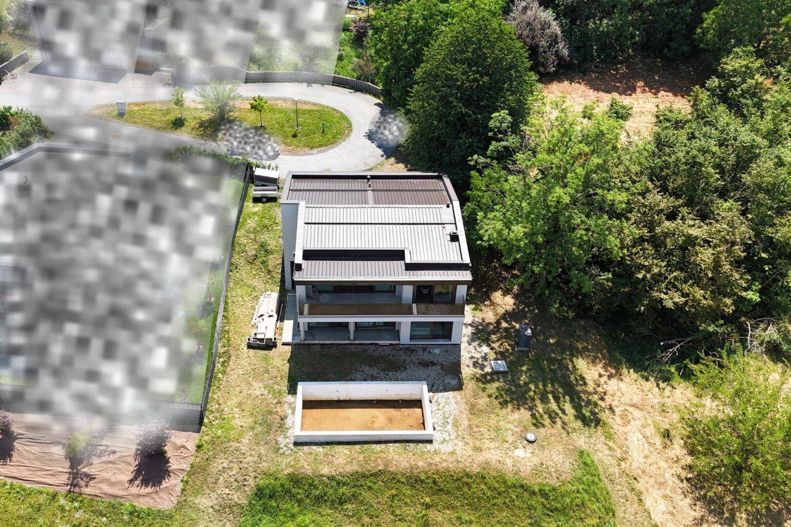 Luftaufnahme des modernen Hauses mit Flachdach, Poolbereich und umgebender Natur.