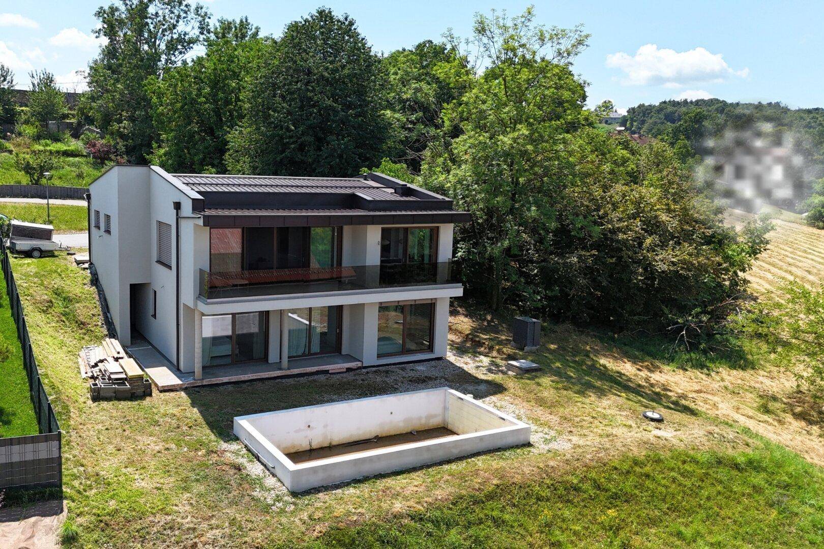 Weitläufige Luftaufnahme des modernen Hauses mit Pool und umgebender grüner Landschaft.