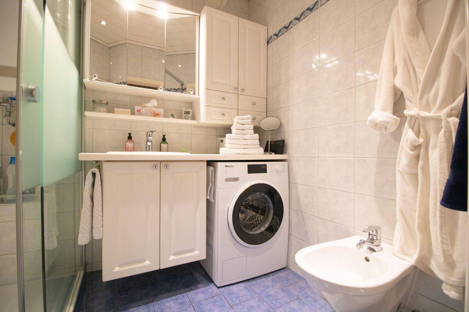 Badezimmer mit Dusche, Waschbecken, Bidet und praktischer Waschmaschine unter dem Waschtisch.