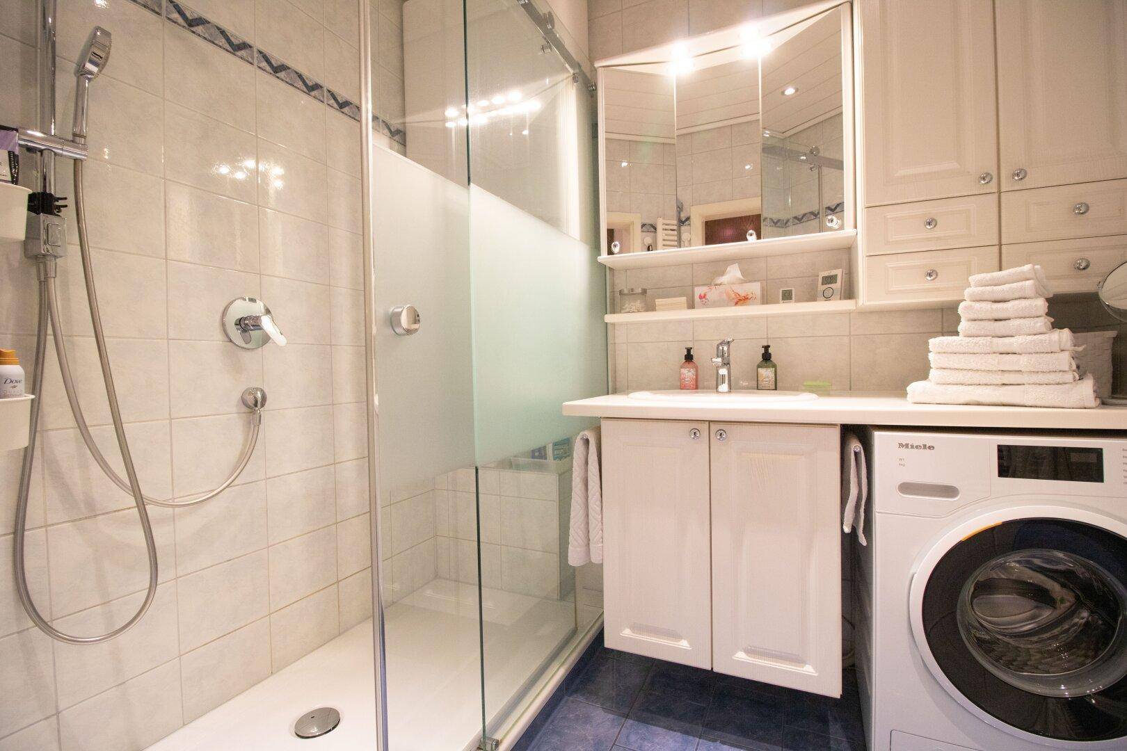 Modernes Badezimmer mit Dusche, Waschbeckenunterschrank und integrierter Waschmaschine.
