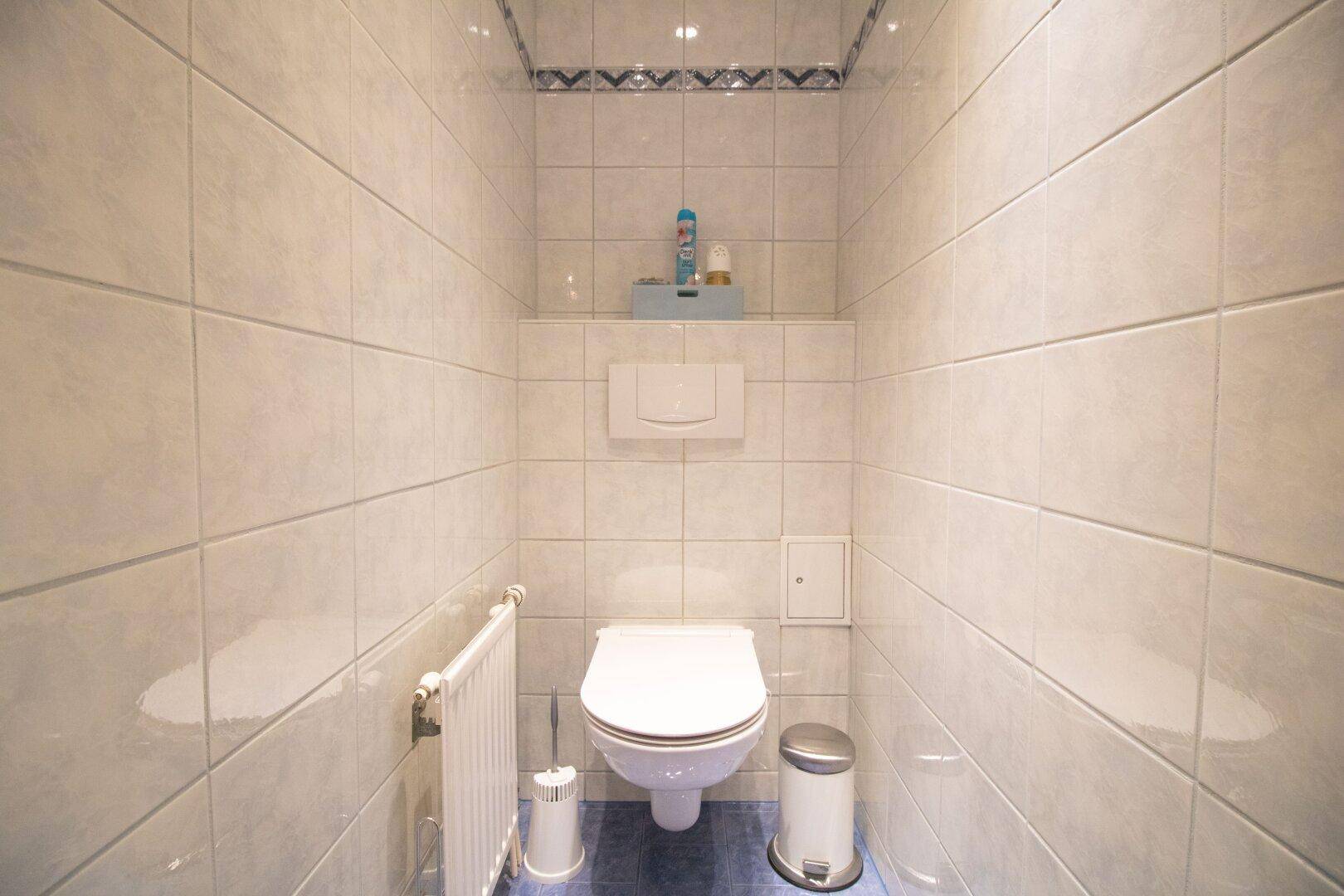 Separate Toilette mit Wand-WC, Fliesenboden und Heizkörper.