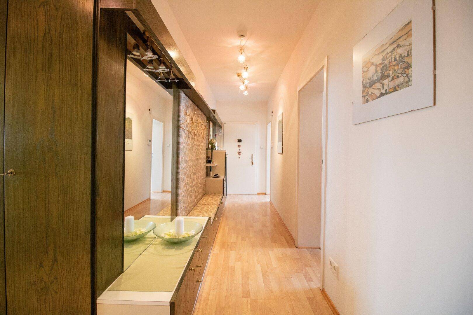 Langer Flur mit hellem Holzboden, Spiegelgarderobe und Zugang zu weiteren Räumen.