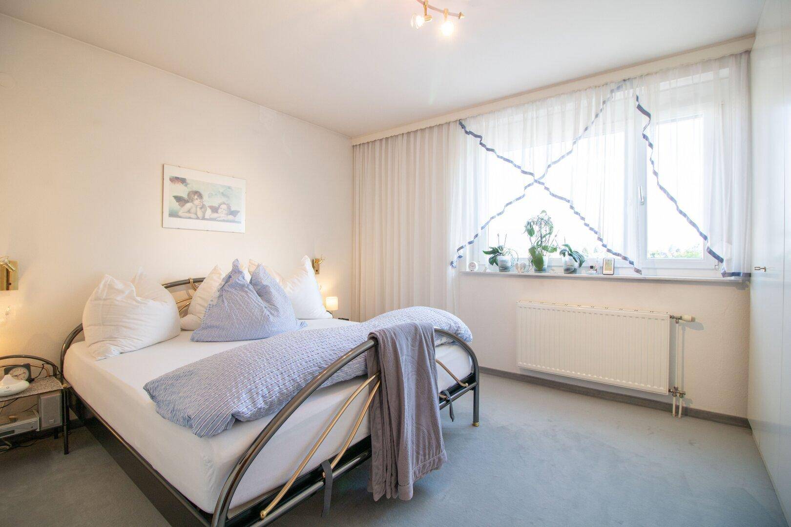 Schlafzimmer mit Doppelbett, Teppichboden und großem Fenster für viel Tageslicht.