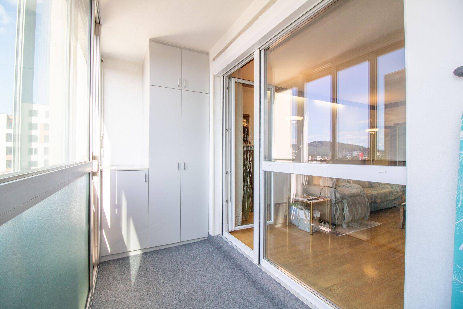 Helle Loggia mit integrierten Schränken, Teppichboden und weitem Ausblick.