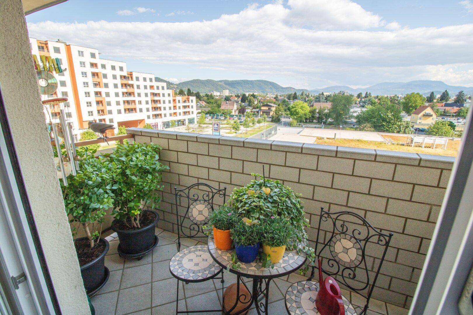 Balkon mit Sitzgelegenheiten, Pflanzen und Panoramablick auf die Stadt und Berge.