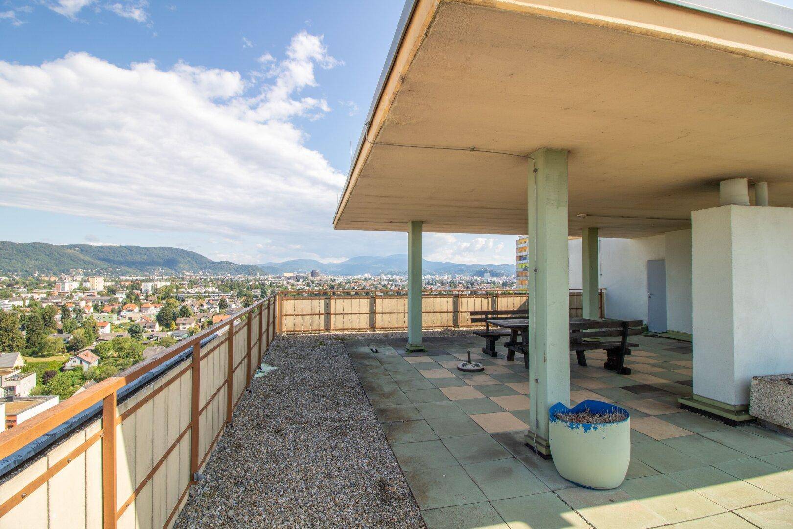 Gemeinschaftliche Dachterrasse mit Sitzgelegenheiten und beeindruckendem Blick auf die Stadt und die Berge.