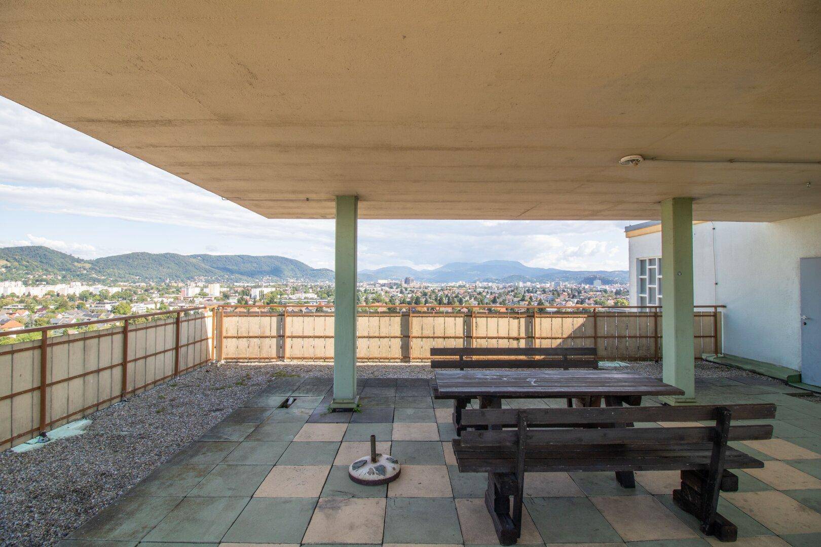 Überdachte Dachterrasse mit rustikalen Holzbänken und weitem Blick auf die umliegende Stadt.