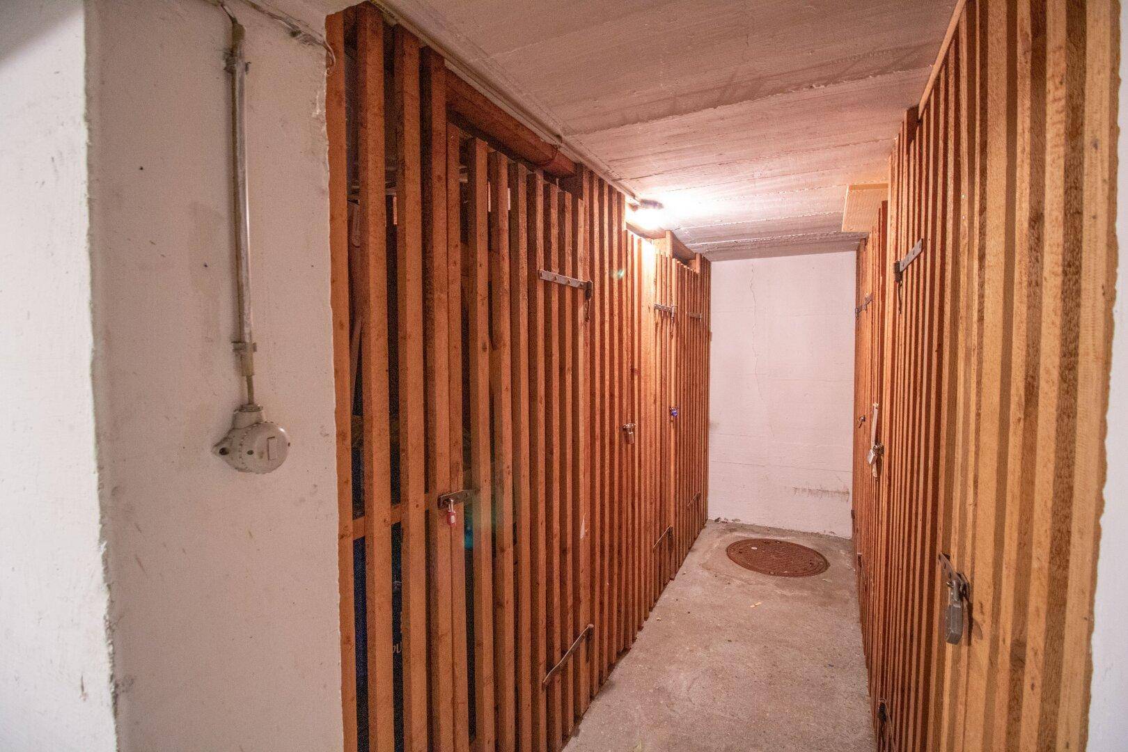 Kellerabteile mit Holzlattenwänden in einem Gemeinschaftskeller, ideal für zusätzlichen Stauraum.