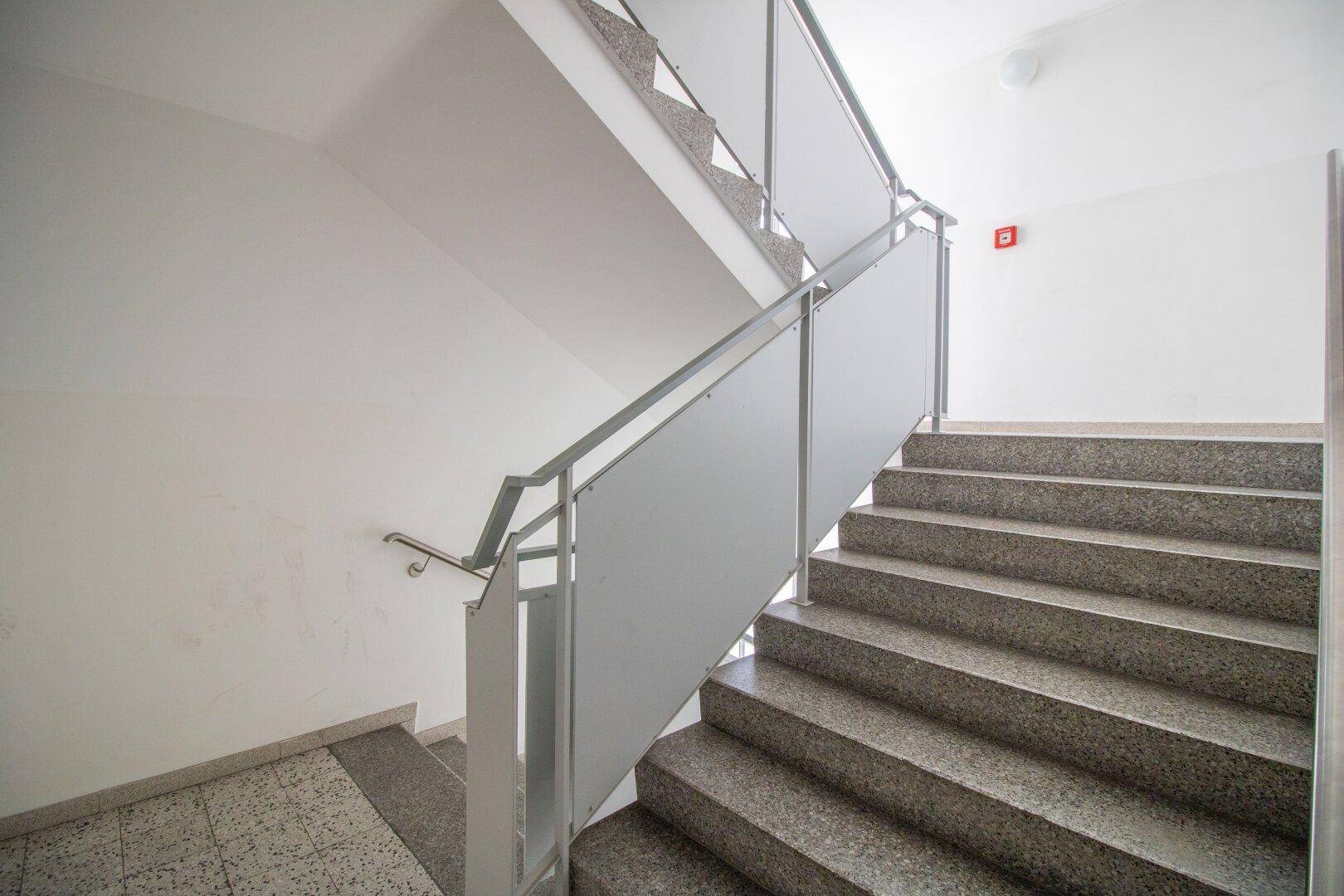 Modernes Treppenhaus mit Granitstufen und Metallgeländer, das die Stockwerke verbindet.