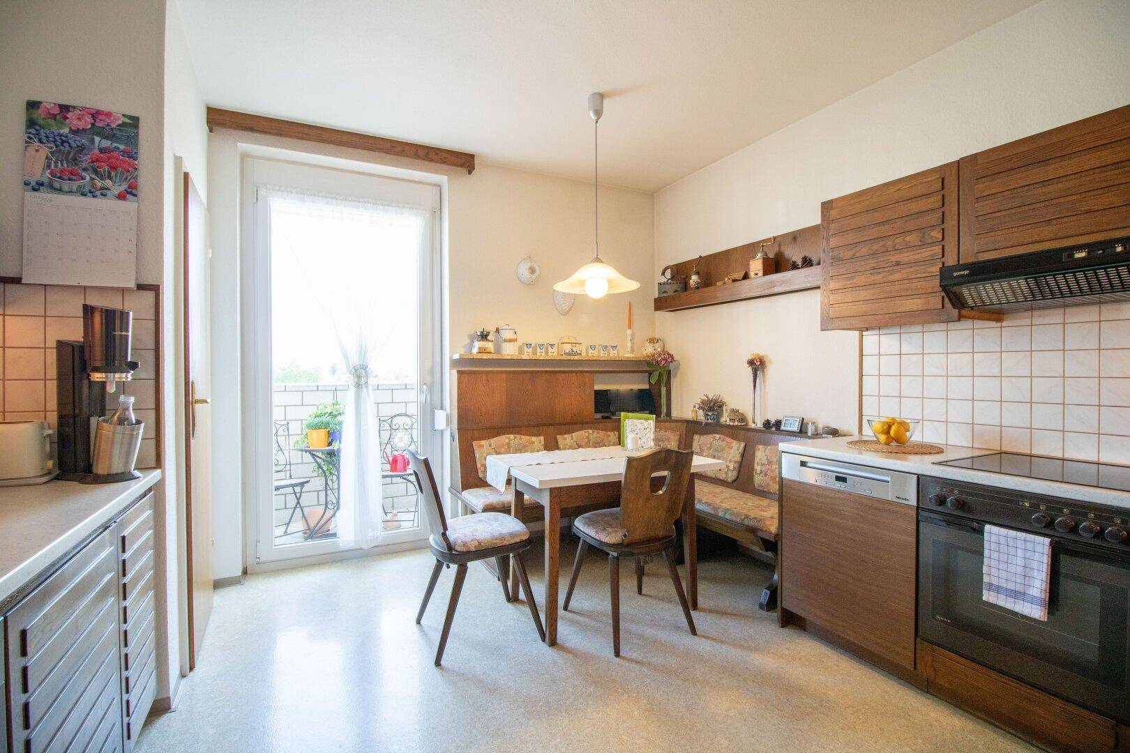 Helle Küche mit Essbereich und Zugang zum Balkon, ausgestattet mit Holzmöbeln.