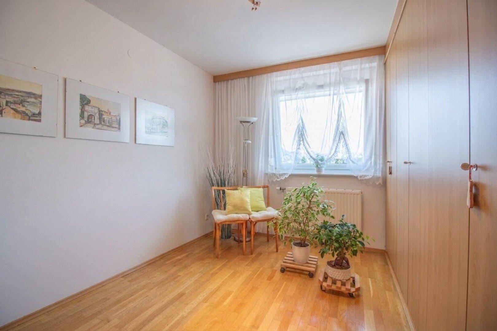 Helles Zimmer mit Holzboden, Fenster und integriertem Kleiderschrank.