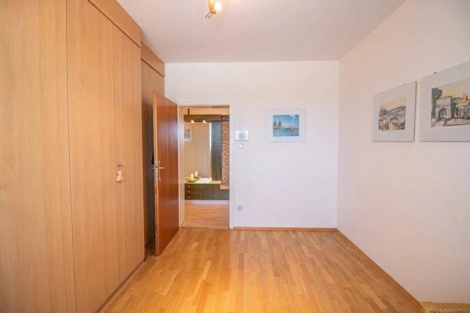 Zimmer mit Holzboden und Einbauschrank, mit Blick in den Flur.