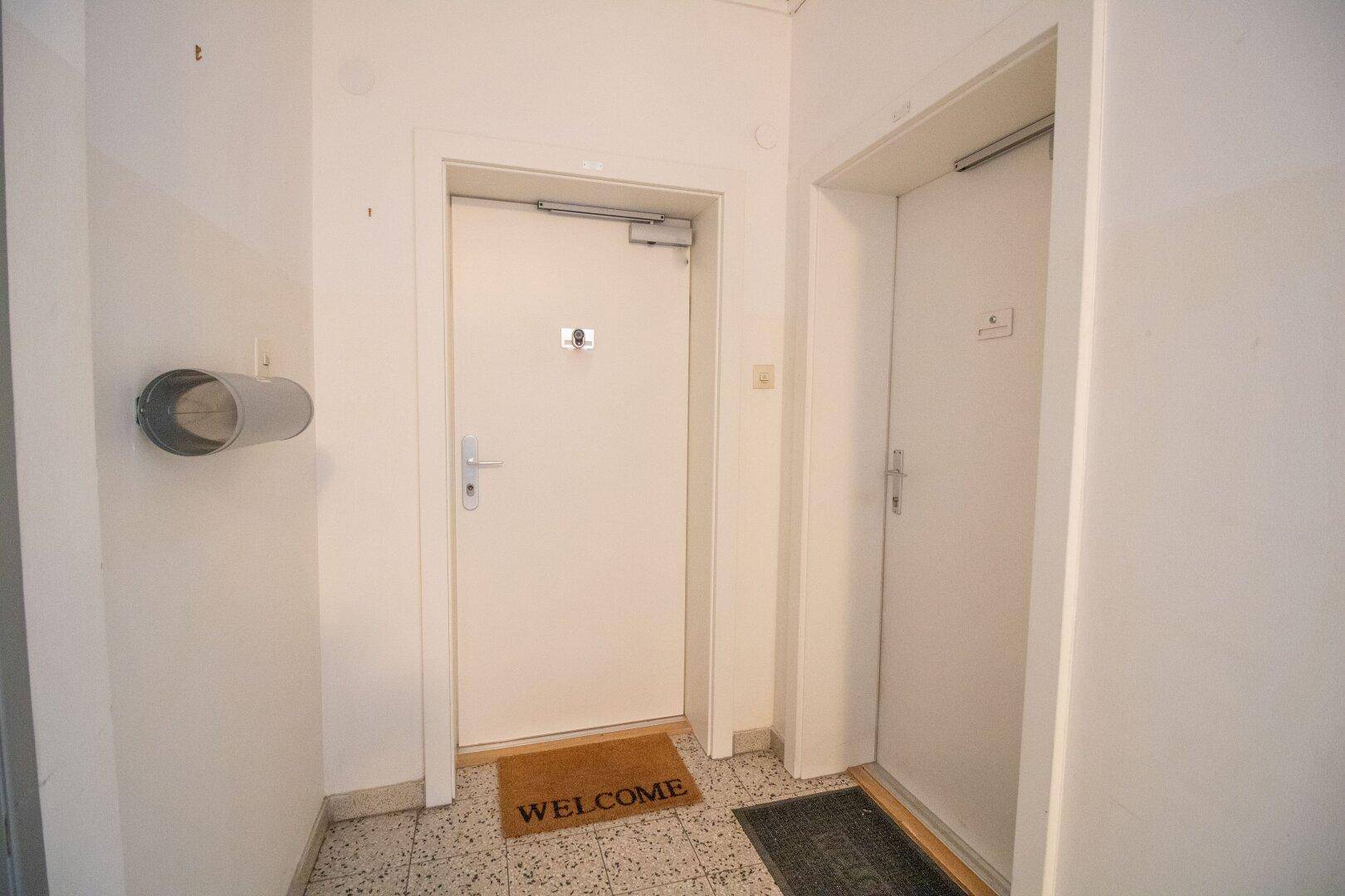 Heller Flur mit zwei Wohnungseingangstüren und Fliesenboden in einem Mehrfamilienhaus.