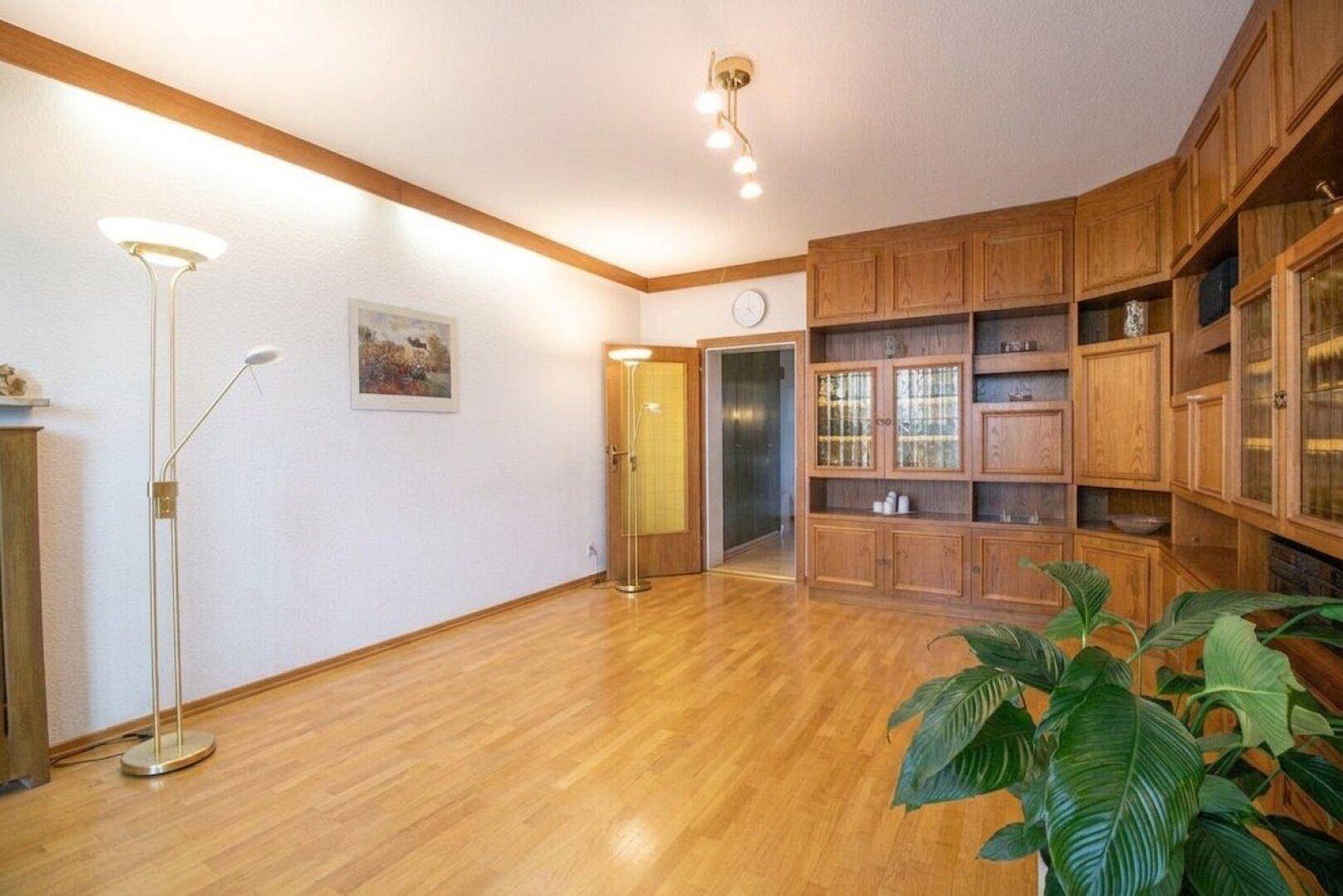 Geräumiges Wohnzimmer mit hellem Parkettboden und einer großen Holzschrankwand.