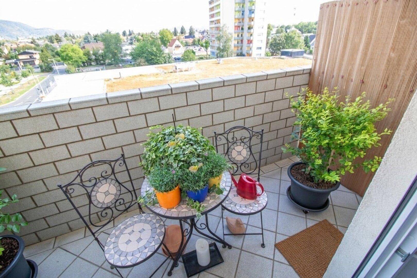 Gemütlicher Balkon mit Fliesenboden, Pflanzen und Blick auf die Stadt und umliegende Gebäude.